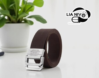 May include: A brown woven belt with a silver-colored buckle. The buckle has a double-bar design and text. The belt is rolled up, showcasing its texture. A potted plant is in the background.