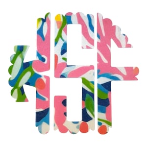 May include: A pink, blue, green and white monogram initial "S" with a scalloped edge. The initial is made of a patterned fabric with a floral design.