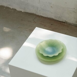 May include: A stack of two glass bowls in shades of green and blue. The top bowl has a scalloped edge and a light blue center. The bowls are sitting on a white surface.
