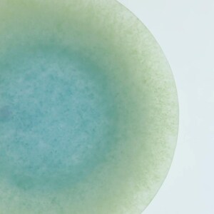 May include: A round, translucent object with a gradient of colors. The center is a light blue, transitioning to a pale green edge. The surface has a slightly textured appearance, set against a white background.