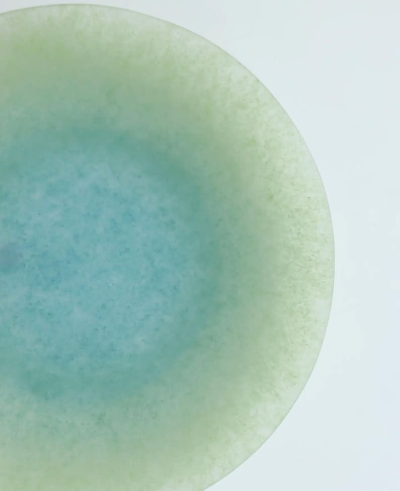 May include: A round, translucent object with a gradient of colors. The center is a light blue, transitioning to a pale green edge. The surface has a slightly textured appearance, set against a white background.