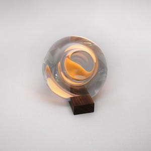 May include: A clear glass sphere with a swirling gold design inside, resting on a dark wooden base.