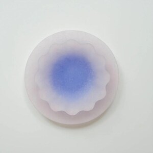 May include: A round, layered object with a soft, blurred appearance. The outer layer is a pale pink, while the center features a vibrant blue hue. The edges of the inner layer have a scalloped design. The object is set against a white background.