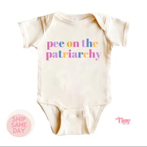 May include: A cream-coloured baby onesie with the text "pee on the patriarchy" in rainbow colours.