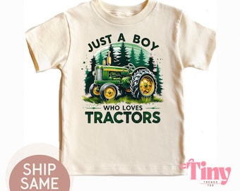 May include: Cream-colored t-shirt featuring a green and yellow tractor graphic with the text "JUST A BOY WHO LOVES TRACTORS". The design includes a forest backdrop. The shirt is a children's apparel item.