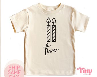 Könnte beinhalten: Ein cremefarbenes T-Shirt mit kurzen Ärmeln und einem schwarzen Motiv aus zwei Kerzen und dem Wort "zwei" in Kursivschrift.