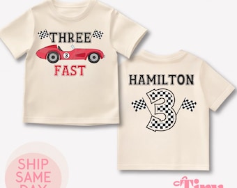 May include: A white t-shirt with a red race car and the text "THREE FAST" on the front. The back of the shirt has the text "HAMILTON" and a checkered flag number "3".