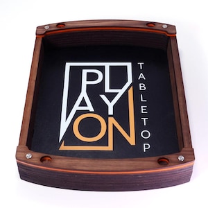 Op de afbeelding: Een houten tabletop gaming tray met de woorden "PLAY ON TABLETOP" in wit en oranje. De tray heeft een donker interieur en oranje rand. Het frame is gemaakt van donker hout.