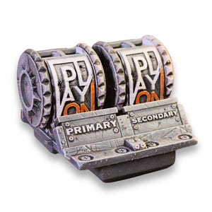 May include: A grey, weathered-looking mechanical gaming accessory featuring two cylindrical rollers labelled PLAY ON. A front panel is divided into two sections labelled PRIMARY and SECONDARY, with visible screw details and a textured, industrial finish.