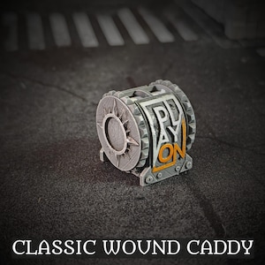 Puede incluir: Un Classic Wound Caddy cilíndrico gris con un diseño de estrella solar en un lado y las palabras "PLAY ON" en blanco y naranja en el otro. El caddy está hecho de un material texturizado y se encuentra sobre una superficie oscura.