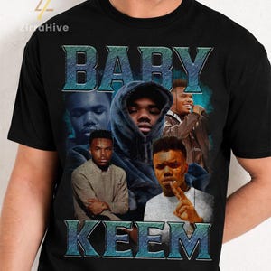 May include: Black t-shirt featuring a collage of images of Baby Keem with the text "BABY KEEM" in a blue, vintage-style font. The design includes multiple portraits of the artist in various poses, creating a unique graphic.