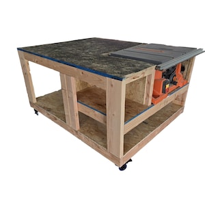 May include: A wooden workbench with a built-in table saw. The workbench has a dark speckled top, a light wood frame, and a lower shelf. The table saw is orange and gray. The workbench is on wheels.