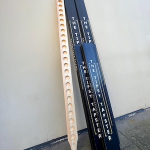 May include: A wooden beer tapster with 20 holes for pouring beer. The tapster is next to three black boxes with the text "The Tipsy Tapster" printed on them.