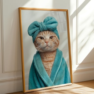 May include: A framed print featuring a cat wearing a teal spa robe and matching head wrap. The cat has orange and white fur and is looking directly at the viewer. The frame is a light brown color.