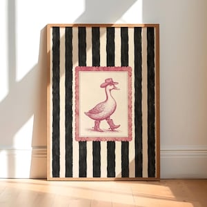 Puede incluir: Una lámina de arte enmarcada con una ilustración central de un pato con sombrero de vaquero y botas, encerrada en un borde rosa festoneado. El fondo consiste en rayas verticales negras y color crema, todo dentro de un marco de madera.