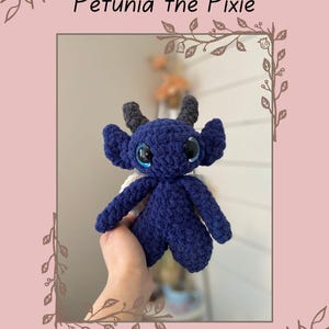 May include: Petunia the Pixie, a crocheted blue and white plush toy with large blue eyes. The toy is being held by a hand. The image includes the text "@lilyclucksncrafts".