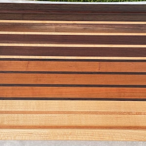 May include: A rectangular wooden cutting board with a variety of wood tones, including light tan, medium brown, and dark brown. The board has a juice groove around the perimeter and is made of multiple horizontal strips of wood.