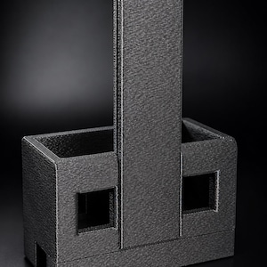 May include: A dark gray, rectangular, 3D-printed organizer with a textured surface. It features a tall, central vertical divider that extends above the main body, two open compartments on either side, and two square cutouts on the front face.