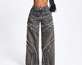 May include: Wide-leg denim jeans in a faded blue wash featuring a high-waisted fit, a horizontal belt-like strap across the hips, and multiple diagonal panels with raw, frayed edges throughout the front of the legs and waistline.