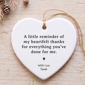 May include: A white heart-shaped ceramic ornament featuring black printed text that reads: A little reminder of my heartfelt thanks for everything you’ve done for me. Below the text is a small heart icon and the name With Love Sarah.