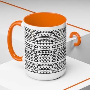 May include: White ceramic mug with an orange interior, handle, and accent. The mug features a black and white geometric pattern around the exterior. The mug is a standard size for coffee or tea.