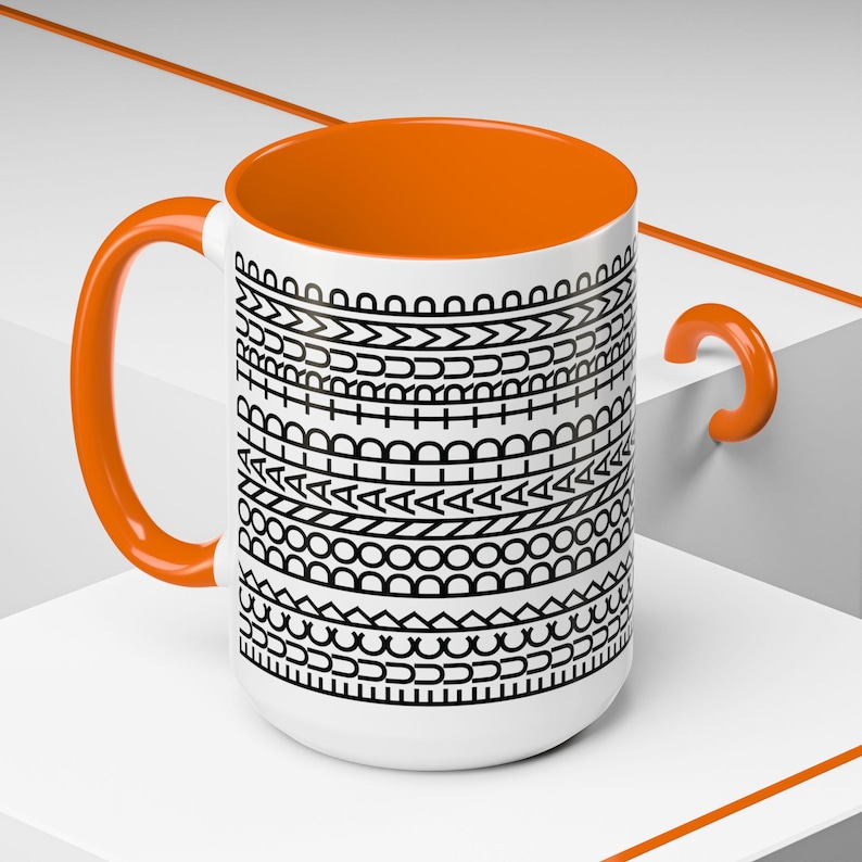 May include: White ceramic mug with an orange interior, handle, and accent. The mug features a black and white geometric pattern around the exterior. The mug is a standard size for coffee or tea.