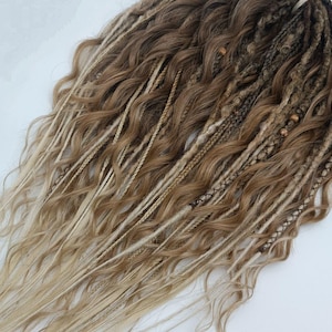 May include: A set of long, wavy synthetic dreadlocks in shades of blonde and brown. The dreadlocks are tied together at the top with a rubber band.