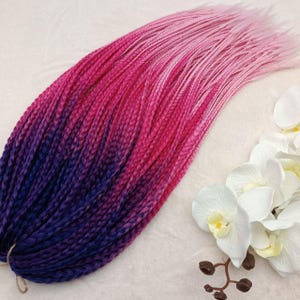 May include: A pack of pre-braided synthetic hair extensions in a ombre color pattern. The hair is dark blue at the roots, transitioning to purple, then pink, and finally light pink at the ends.