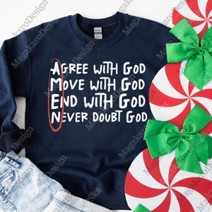 May include: Navy blue sweatshirt with white text: "Agree with God, Move with God, End with God, Never Doubt God." A red oval highlights the word "Amen." Decorative red and white peppermint candies and green bows are in the background.