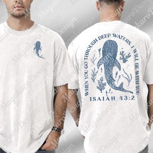 Puede incluir: Camiseta blanca con un diseño de tiburón ballena azul. La parte delantera tiene un pequeño gráfico de tiburón ballena, mientras que la parte trasera muestra un diseño más grande con el texto "WHEN YOU GO THROUGH DEEP WATERS, I WILL BE WITH YOU. ISAIAH 43:2."