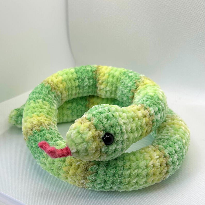 May include: A green and yellow crocheted snake toy with a pink tongue and black eyes.