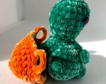 May include: A green crocheted plush toy with a single blue eye, sitting next to an orange crocheted basket.