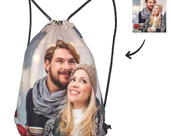 May include: A drawstring bag with a photo of a couple printed on it. The photo shows a man and a woman standing close together, smiling. The bag is white with black drawstrings.