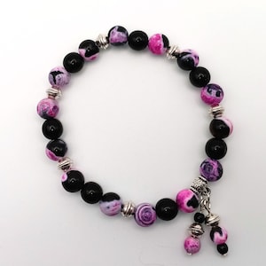 May include: A black and pink beaded bracelet with silver accents. The bracelet has a charm with two dangling pink and black beads.