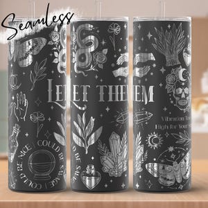 May include: Three black stainless steel tumblers with silver illustrations of celestial and botanical elements. The text "Let Them" is displayed in silver. The tumblers feature a variety of designs, including a skull, crystals, and a moth.