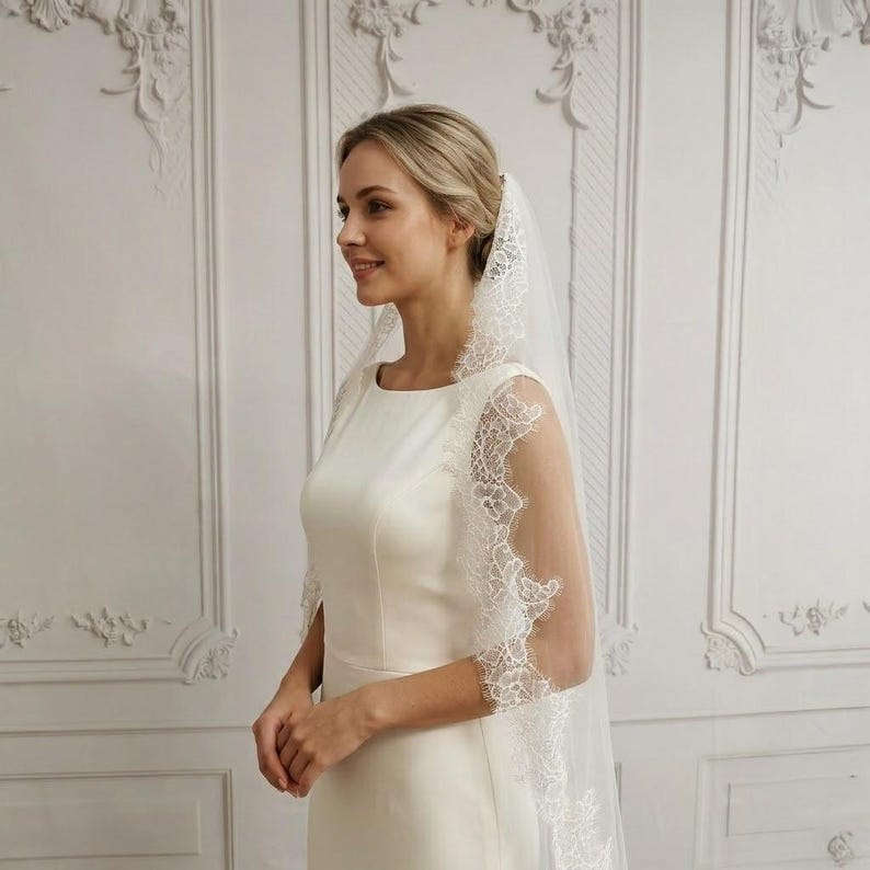May include: A bride wearing a white wedding dress and a matching veil with delicate lace trim. The veil drapes over the shoulders and arms, creating an elegant and romantic look. The dress is simple and classic.