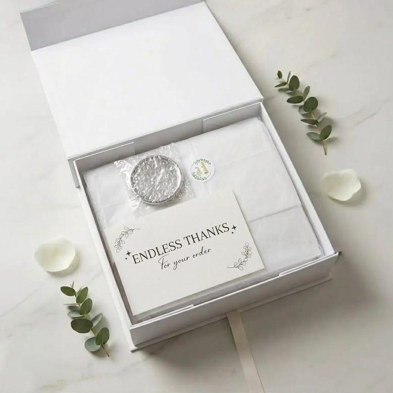 May include: A white gift box with an open lid, revealing a silver item in a plastic wrapper, a card with the text "ENDLESS THANKS For your order", and a small sticker. The box is lined with white tissue paper and decorated with greenery.