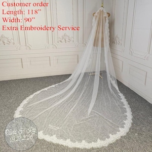 May include: A long, white bridal veil with delicate lace trim. The veil is displayed on a mannequin, showcasing its length of 118 inches and width of 90 inches. The veil has a scalloped lace edge and features custom embroidery.
