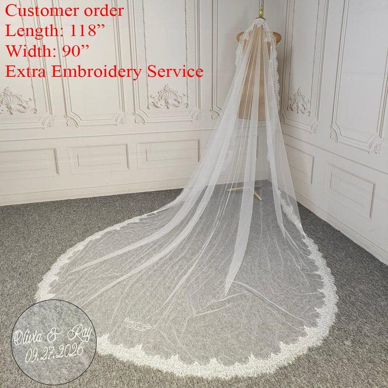 May include: A long, white bridal veil with delicate lace trim. The veil is displayed on a mannequin, showcasing its length of 118 inches and width of 90 inches. The veil has a scalloped lace edge and features custom embroidery.