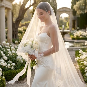 May include: A floor-length white wedding veil featuring intricate lace trim along the edges, paired with a strapless white satin gown and a bouquet of white tulips and roses tied with long white ribbons, creating a classic bridal ensemble.