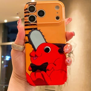 Puede incluir: Funda de teléfono naranja con un personaje de dibujos animados que sostiene una motosierra y una pajarita negra. La funda tiene un recorte para la cámara y un diseño de rayas negras y naranjas en la parte superior.