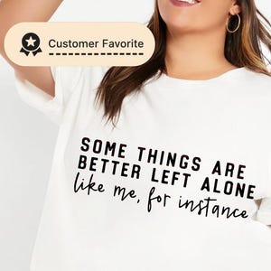 Puede incluir: Camiseta blanca con el texto "SOME THINGS ARE BETTER LEFT ALONE like me, for instance" en negro. La camiseta es la favorita del cliente. La modelo lleva pantalones cortos vaqueros.