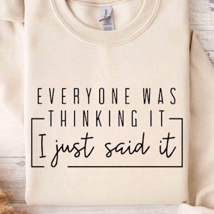 May include: A cream-colored sweatshirt with the text "EVERYONE WAS THINKING IT - I just said it" in black. The text is centered and framed by a black rectangle. The sweatshirt has a crew neck and long sleeves.