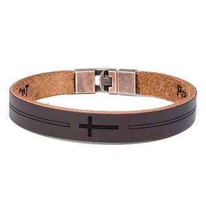 May include: A brown leather bracelet with a silver clasp and a black cross engraved on the leather.