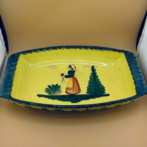Könnte beinhalten: Rechteckige Servierschale aus Keramik mit gelbem Innenraum und dunkelblauem Rand. Die Schale zeigt eine handgemalte Szene einer Frau in traditioneller Kleidung, die Blumen hält, mit einem grünen Baum und Büschen.