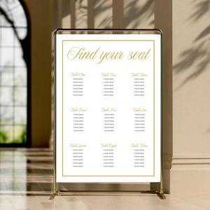 Könnte beinhalten: Ein goldfarbener, metallgerahmter Sitzplan mit den Worten "Find your seat" in eleganter Schrift. Die Tafel ist in neun Abschnitte unterteilt, die jeweils mit einer Tischnummer und Platz für Gästenamen versehen sind. Der Hintergrund ist neutral.