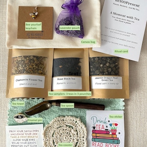 May include: A tea gift set including a canvas bag, a bee keychain, a purple lavender pouch, a ritual card, three tea samplers labeled Chamomile, Rose Black, and Jasmin Dragon Pearl, a metal tea spoon, an enamel pin, a crochet coaster, and a sticker.