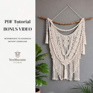Puede incluir: Tapiz de macramé color crema con un diseño geométrico, colgado de una rama de madera. La pieza presenta intrincados nudos y flecos, con borlas a cada lado. La imagen incluye el texto "PDF Tutorial + Bonus Video" y "NessMacrame Studio".