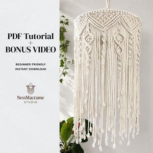 May include: Cream-colored macrame lampshade with geometric patterns and hanging fringe. The lampshade is suspended from a white cord. The text "PDF Tutorial + Bonus Video" and "Beginner Friendly Instant Download" is visible.
