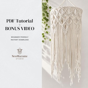 May include: Cream-colored macrame lampshade with diamond and fringe design. The lampshade is suspended from a white cord and hangs against a white wall. Text on the left reads "PDF Tutorial + BONUS VIDEO" and "Beginner Friendly Instant Download".
